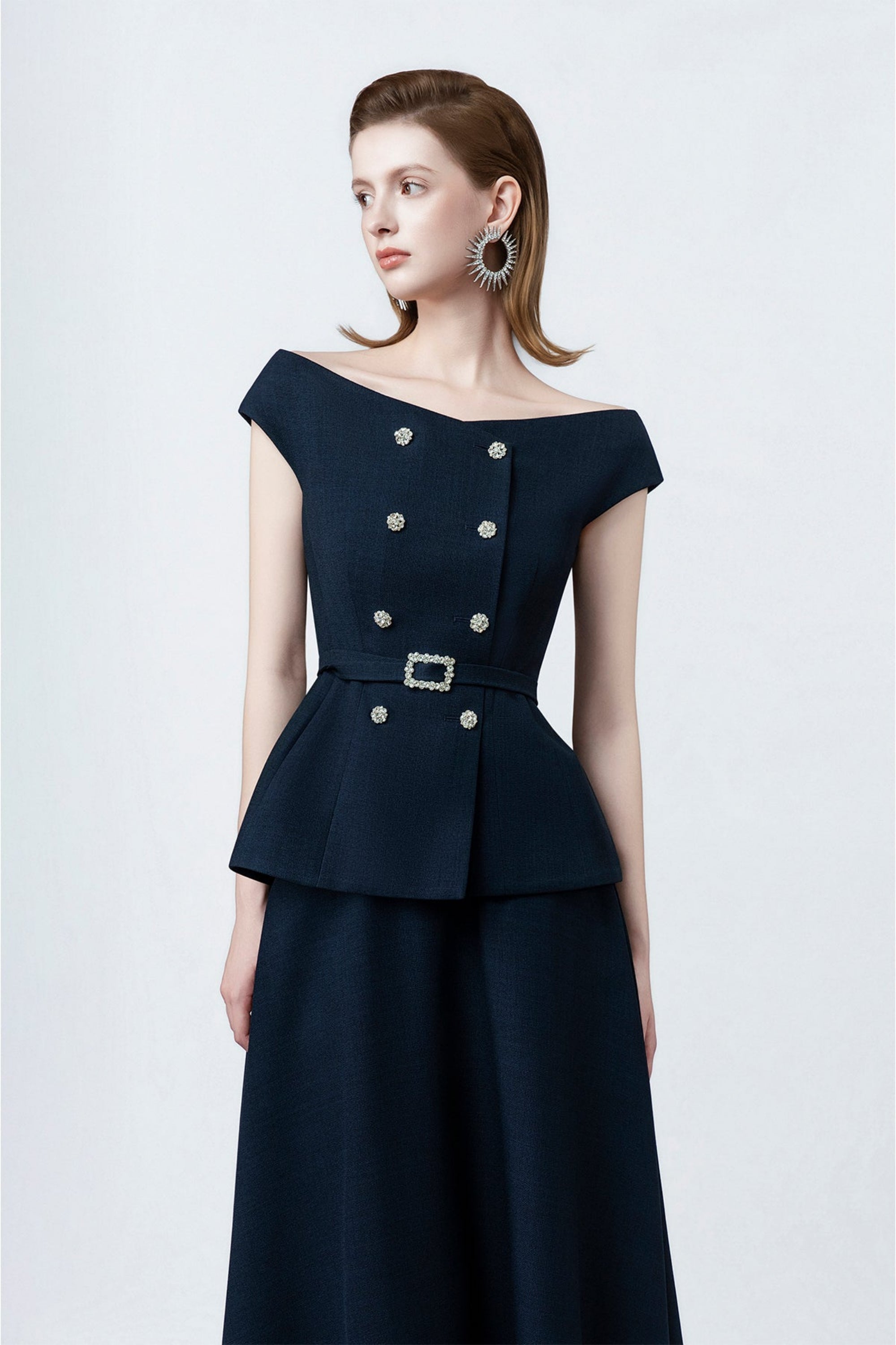 Woman wearing a dark blue dress with silver buttons on a white background