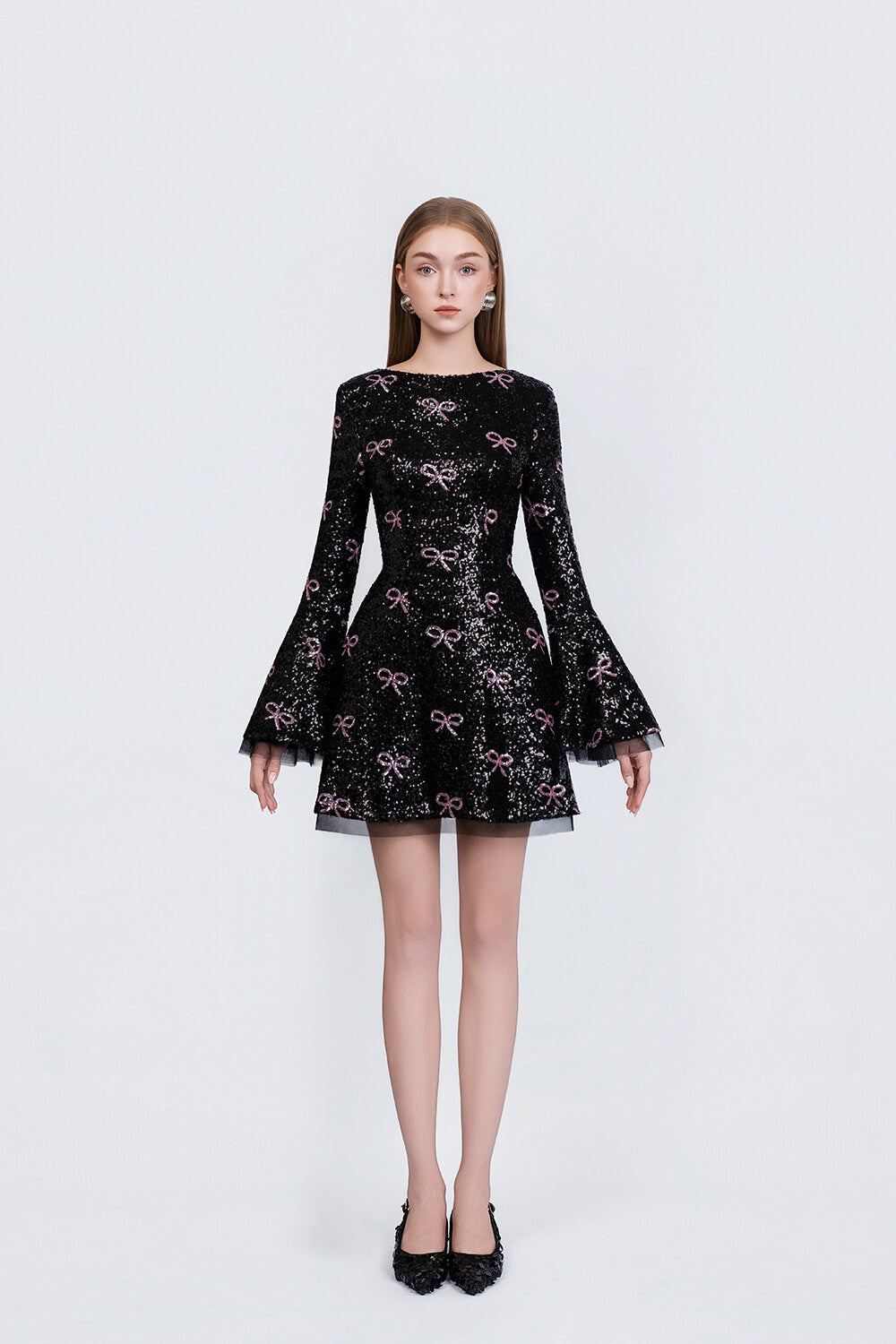 Black dress with pink bow pattern worn by a model on a white background