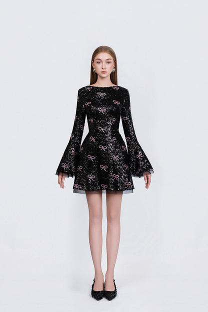 Black dress with pink bow pattern worn by a model on a white background